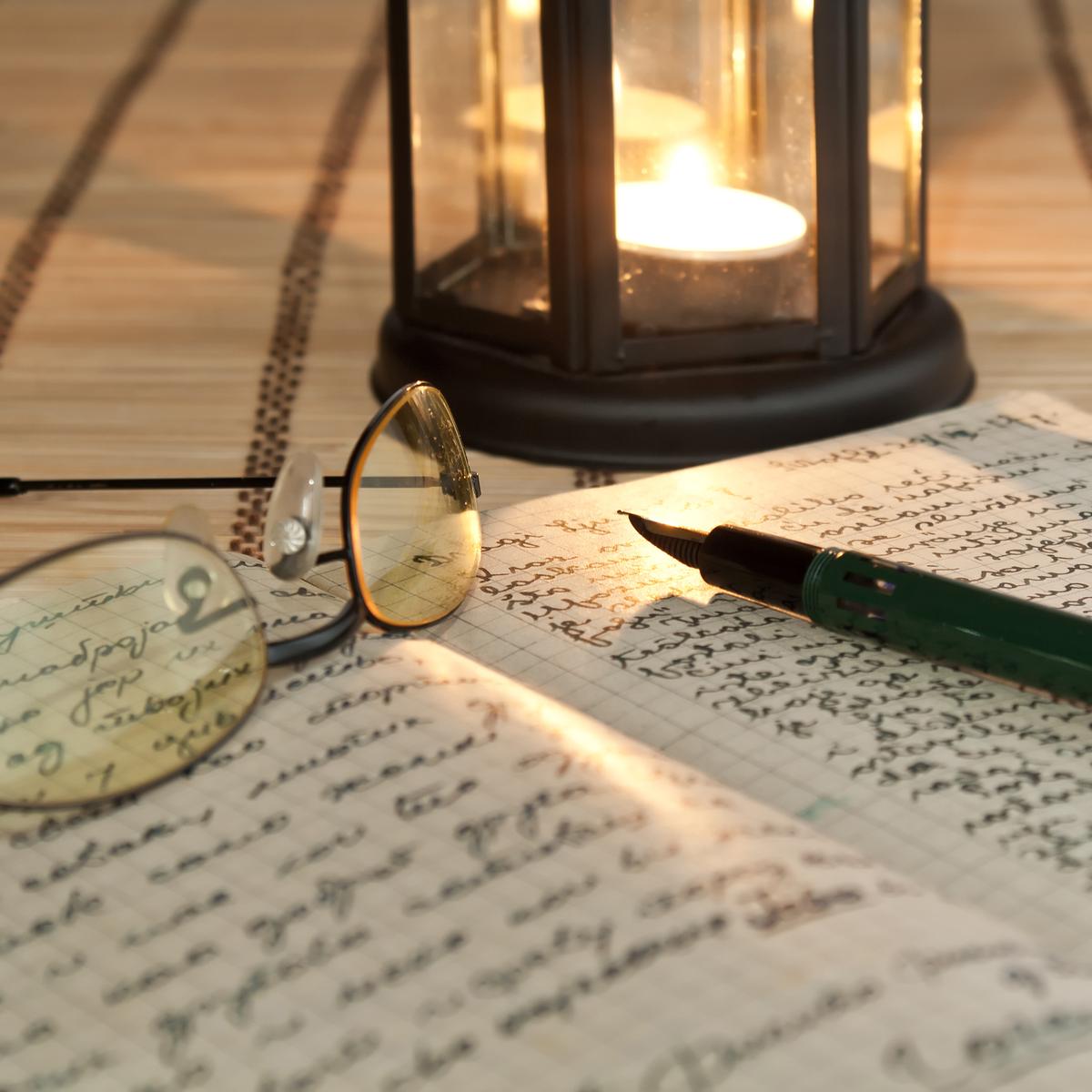 An open journal and reading glasses beside a glowing lantern